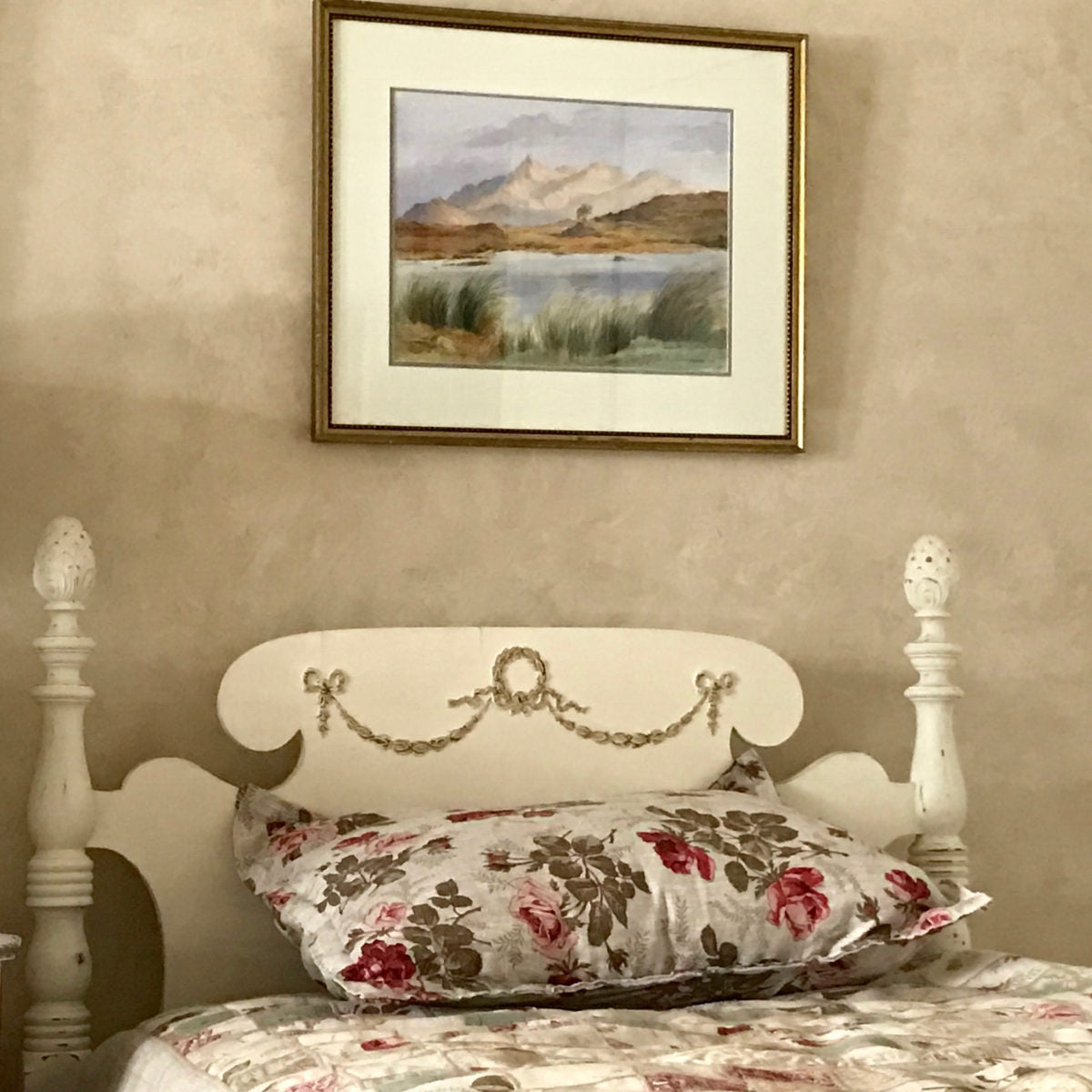 Cream painted spindle bed headboard decorated with a gold Efex flexible moulding bow and swags, with floral bedding and a framed landscape above