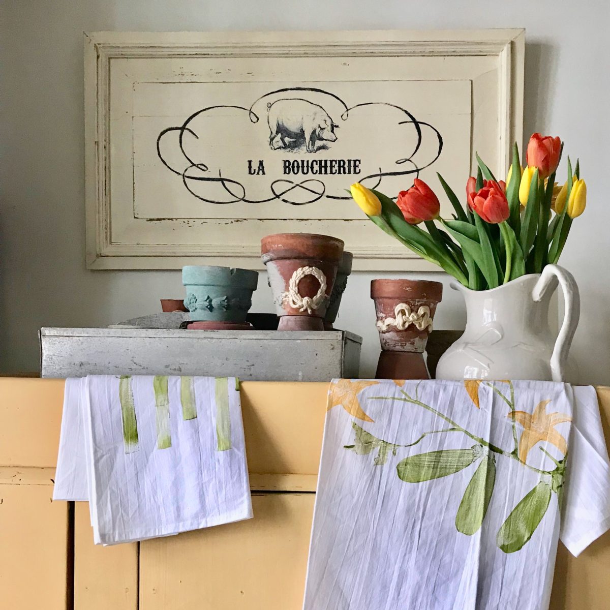 Kitchen vignette with flower pots trimmed in B1 and B14 bow Efex flexible mouldings, tulips in a white pitcher and tea towels on a yellow cabinet