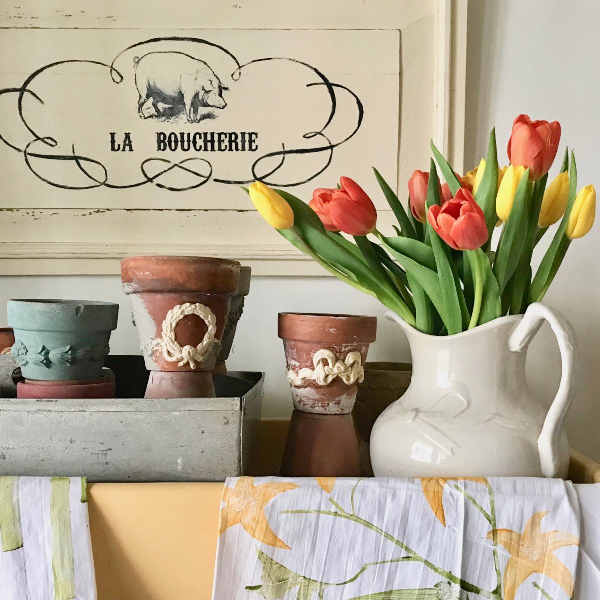 Painted terracotta pots decorated with B14 Ribbed Bow and swag Efex flexible mouldings, beside a white pitcher of tulips and a La Boucherie sign