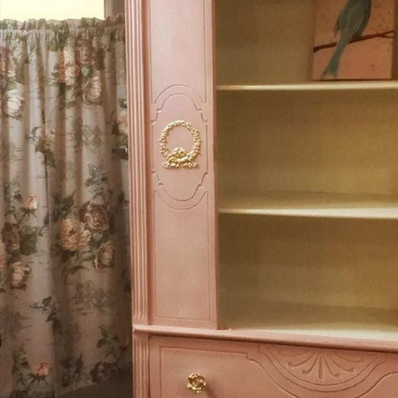 Blush pink painted bookcase cabinet with a gold B21 Leaf Wreath Bow Efex flexible moulding on the side panel, beside floral curtains