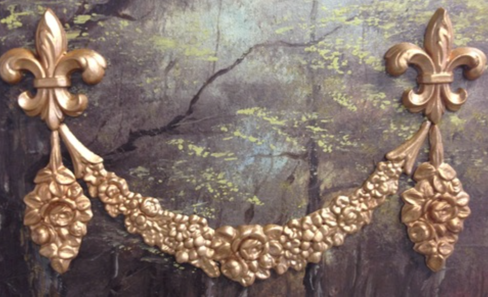 Gilded arrangement of Efex flexible mouldings: two fleur-de-lis with D2 Rose Drops hanging below and a rose garland swag between them, on a dark painted landscape