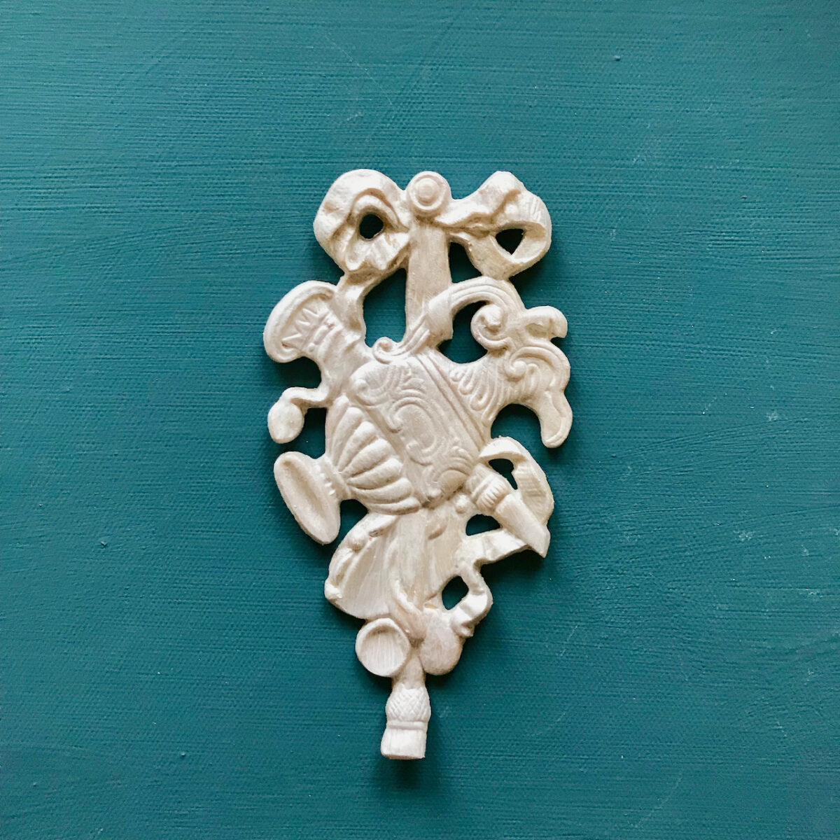 R7 Federal Rosette, an Efex flexible moulding trophy applique of musical instruments and a shield hanging from a ribbon bow, in white on teal