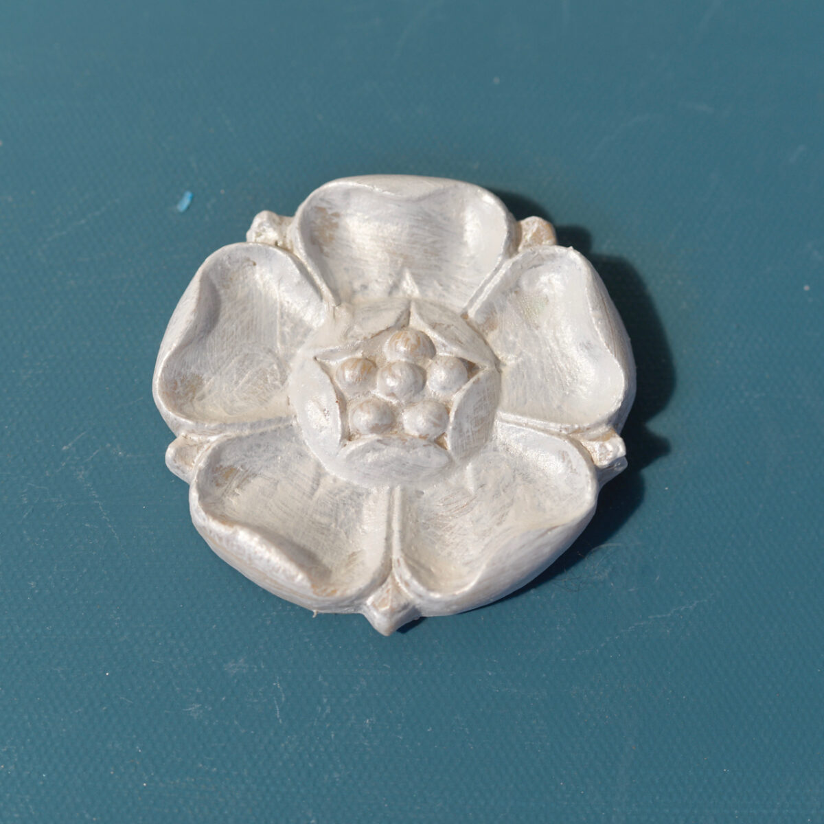 R9 Poppy Rosette, a five-petal Efex flexible moulding flower with a beaded centre in a pearl finish on a teal background