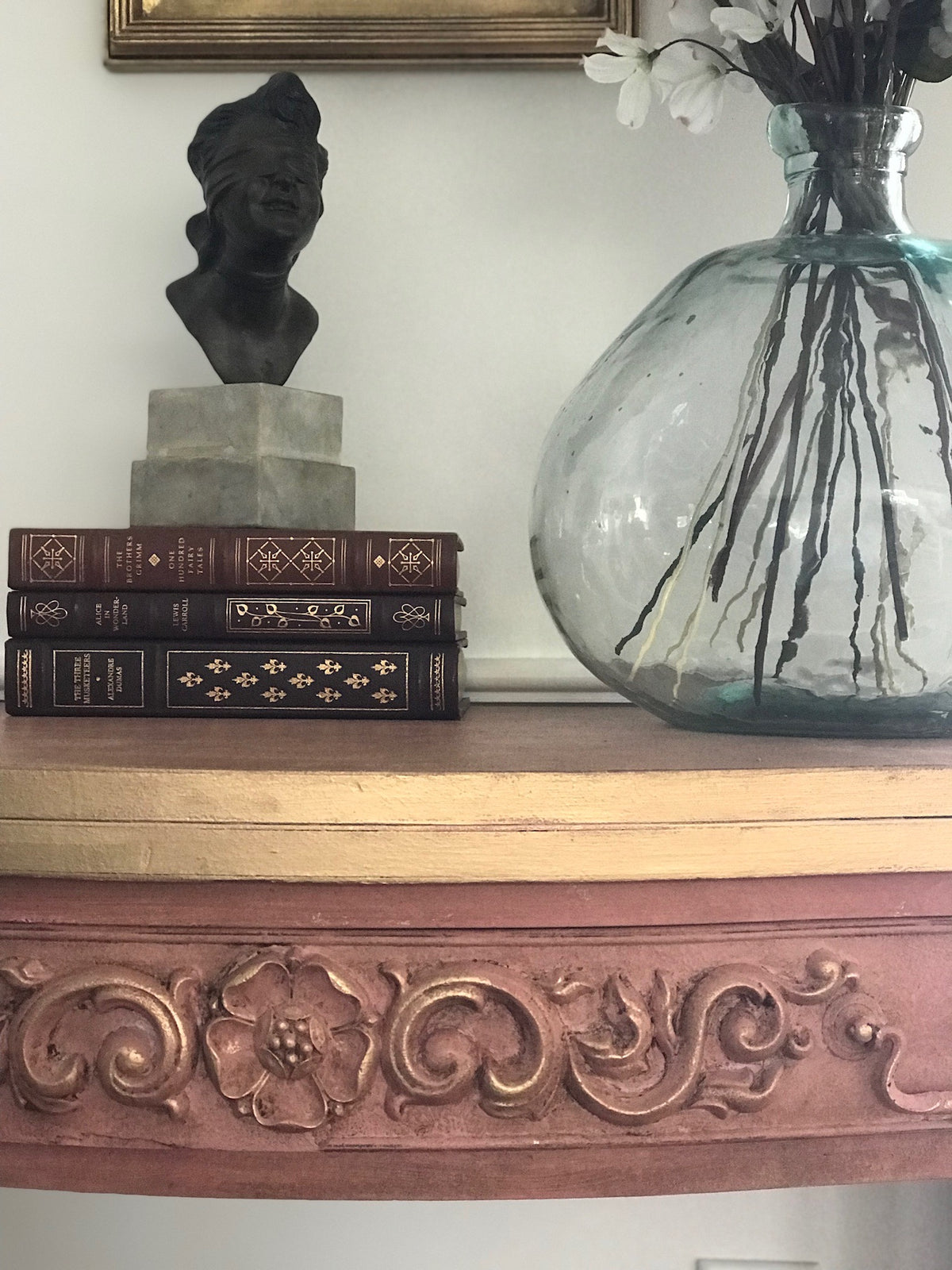 Dusty pink painted chest with R9 Poppy Rosette Efex flexible moulding and leafy scrolls across the top drawer, styled with antique books, a bronze bust and a glass vase