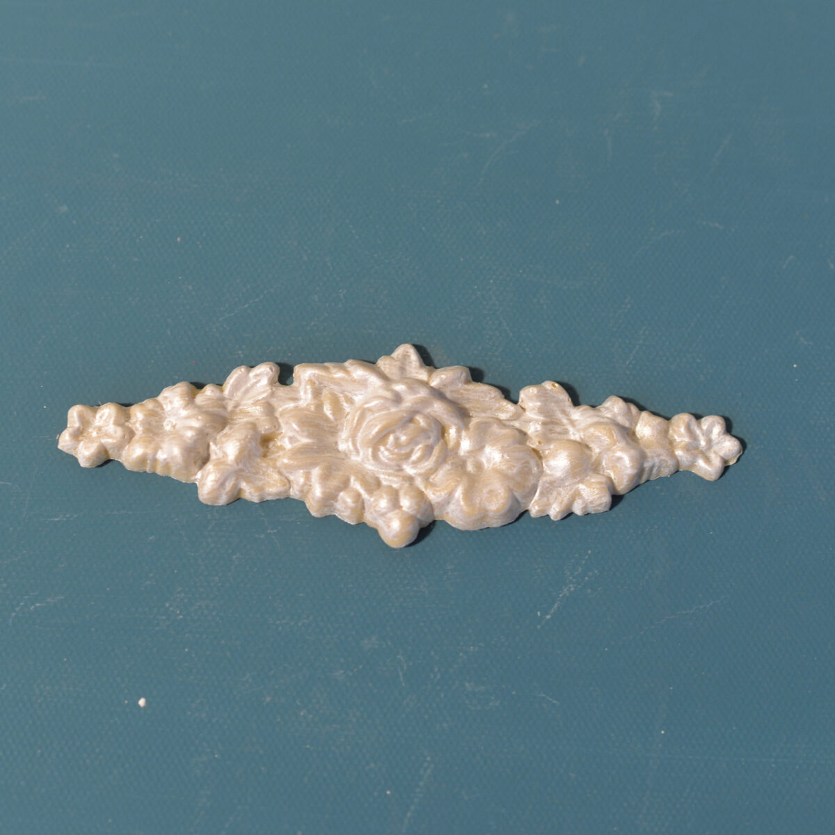 R16 Small Rose Bud Rosette, a slim horizontal Efex flexible moulding of a central rose with buds and blossoms tapering to each side, pearl finish