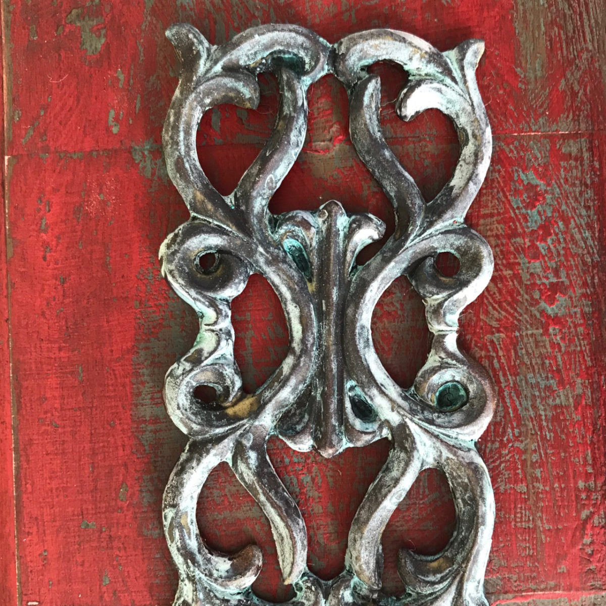 R18 Celtic Rosette, an open-work Efex flexible moulding panel of interlacing Celtic scrolls in antiqued silver on red distressed wood