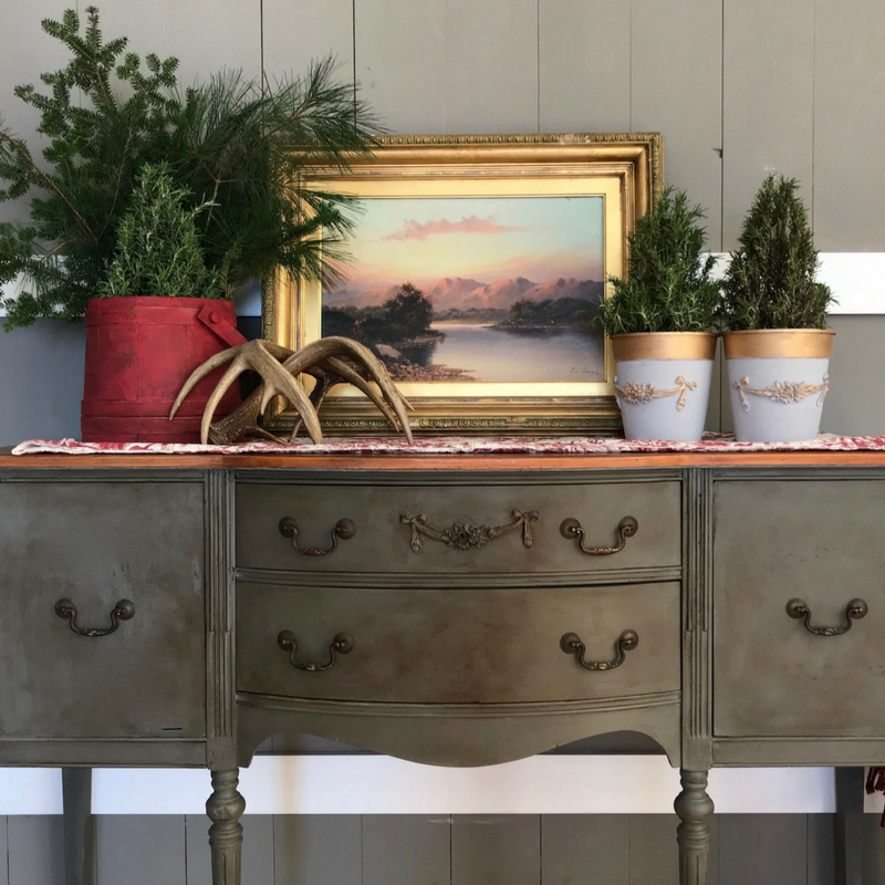 Olive green painted buffet with an SW9 Rose Swag Efex flexible moulding across the top drawer, styled with a landscape painting, antlers and evergreen topiaries