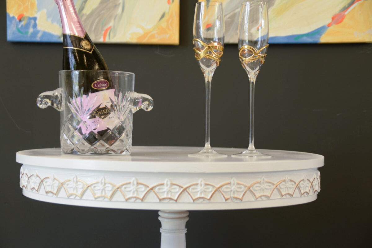 Round white side table edged with T23 Celtic Art Deco Efex flexible moulding, set with champagne in a crystal ice bucket and two gold-rimmed flutes