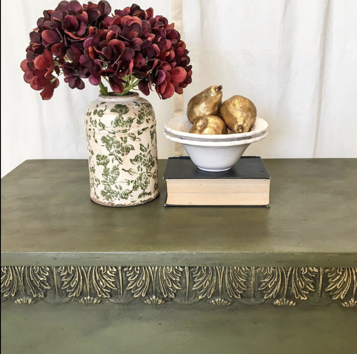 Sage green painted table with T34 Large Acanthus Leaf Efex flexible moulding along the apron, gilded highlights, styled with burgundy hydrangeas and gold pears