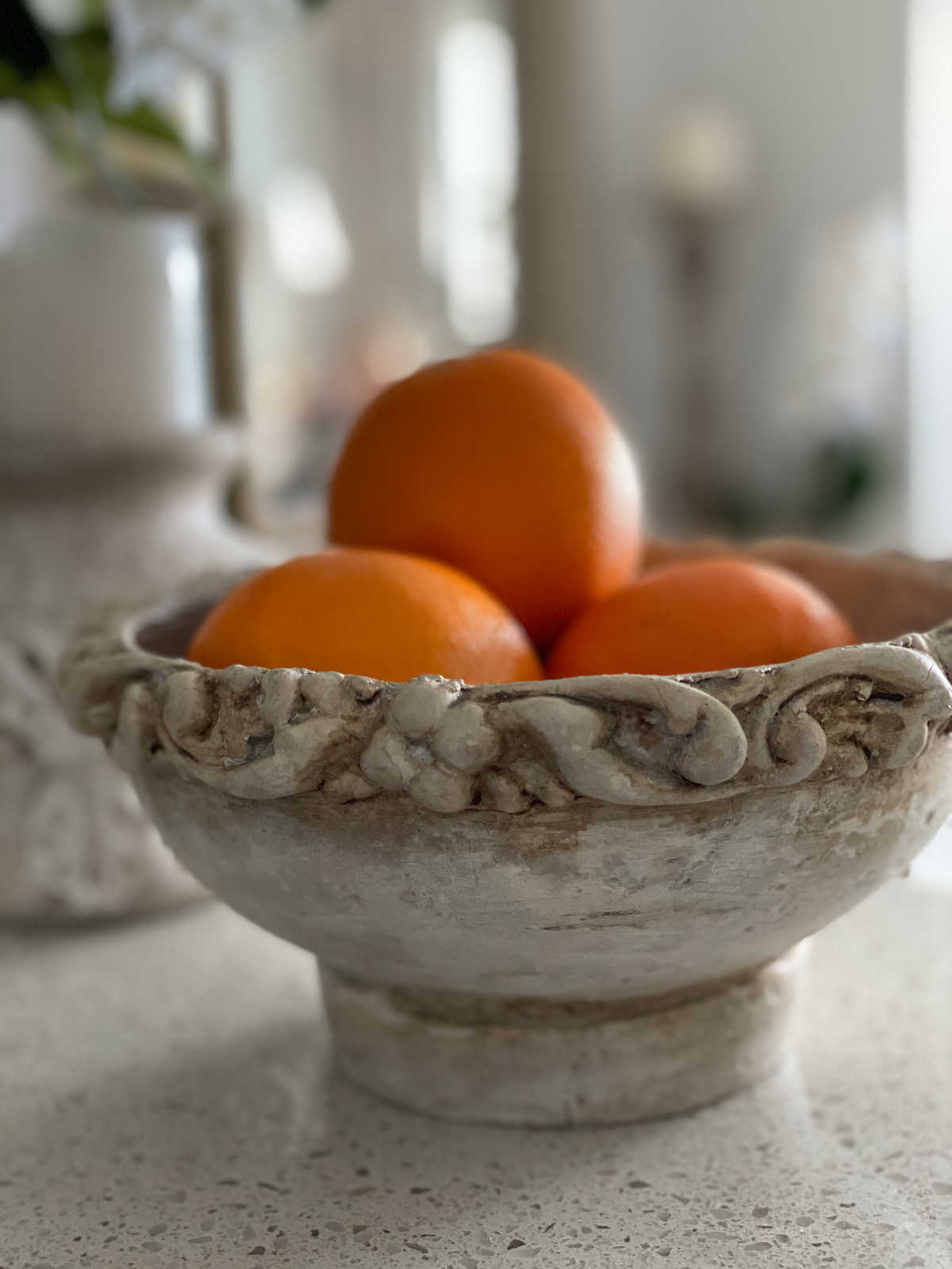 Stone-finish footed bowl of oranges with T36 Leaf Trim Efex flexible moulding wrapped around the rim, shown in a soft-focus kitchen setting